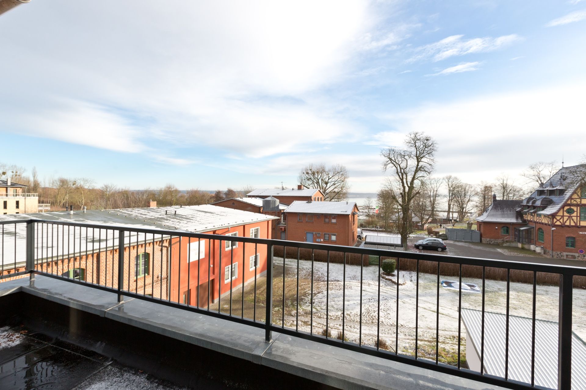 Blick von einem Balkon auf rote Gebäude und eine winterliche Landschaft mit etwas Schnee.