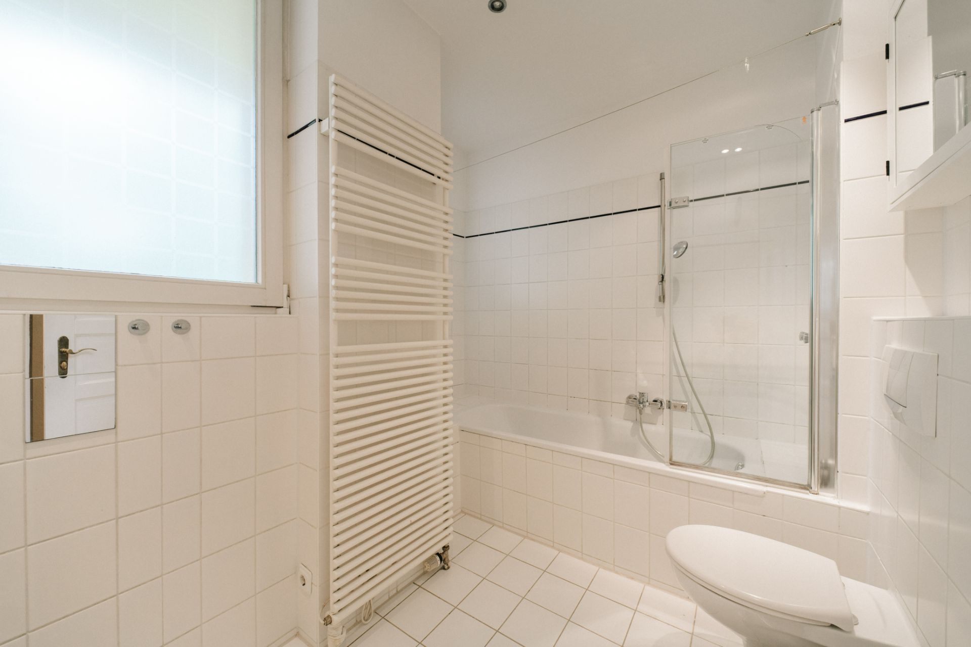 Helles Badezimmer mit Badewanne, Handtuchheizkörper, WC und Fenster.