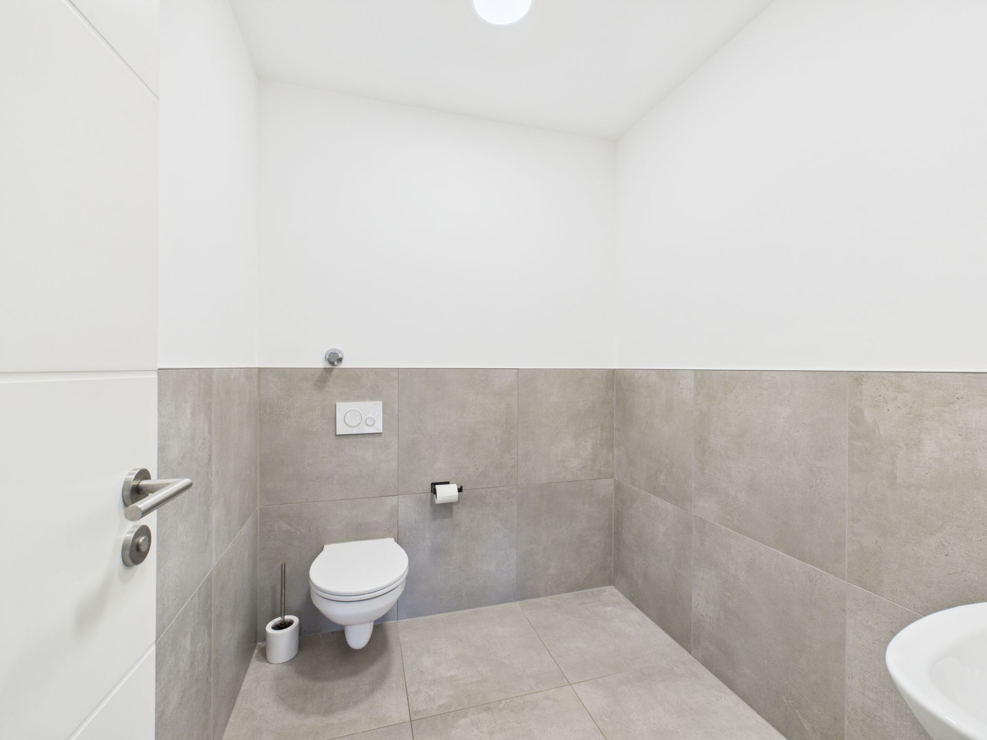 Modernes, schlichtes WC mit grauen Fliesen und weißer Keramiktoilette.