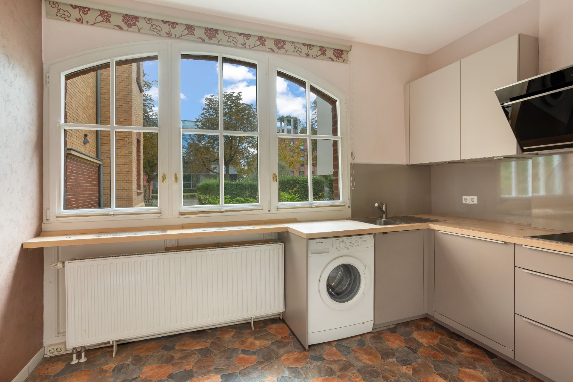 Helle Küche mit großem Fenster, Waschmaschine, Spüle und Einbauschränken.