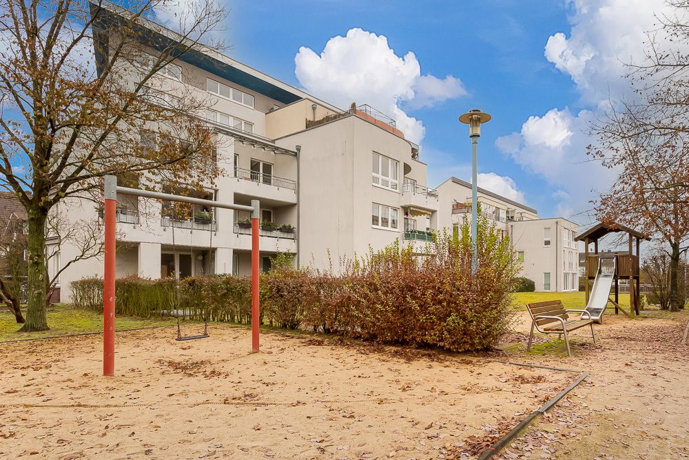 Wohnhaus mit Spielplatz, Schaukel, Rutsche und Bänken im grünen Außenbereich.