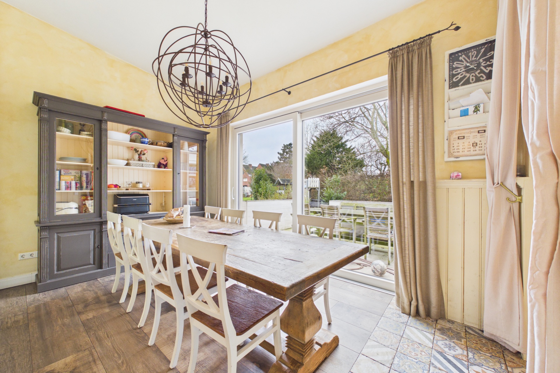 Esszimmer mit großem Holztisch, weißen Stühlen und Blick auf eine Terrasse mit Garten.