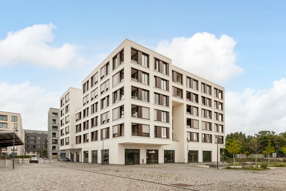 Modernes, mehrstöckiges Wohngebäude mit großen Fenstern und Innenhof, gepflasterter Platz im Vordergrund.