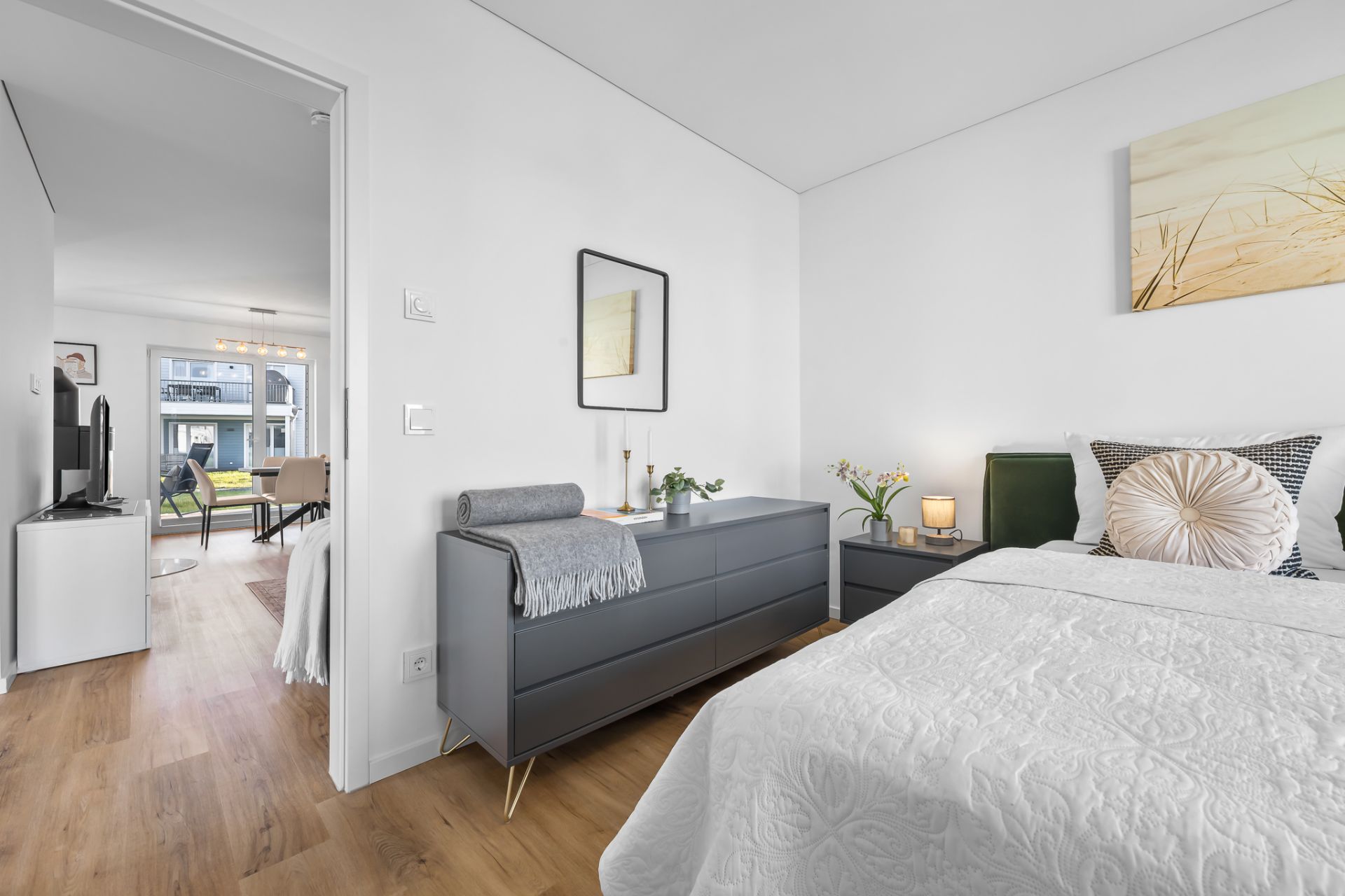 Helles Schlafzimmer mit Doppelbett, Kommode, Nachttisch und Blick ins Wohnzimmer.
