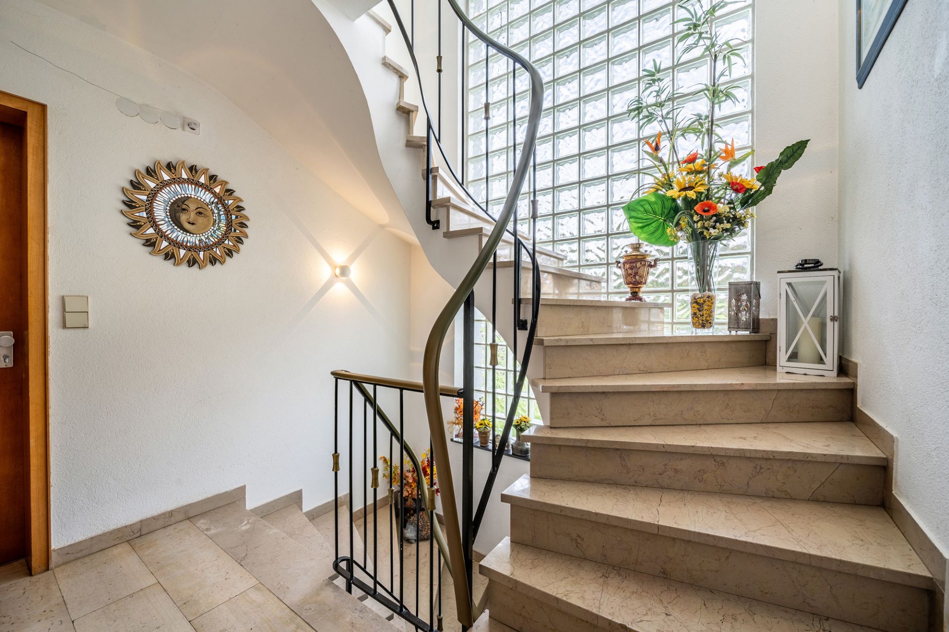 Helles Treppenhaus mit Dekoration, Blumen und Glasbausteinfenster.