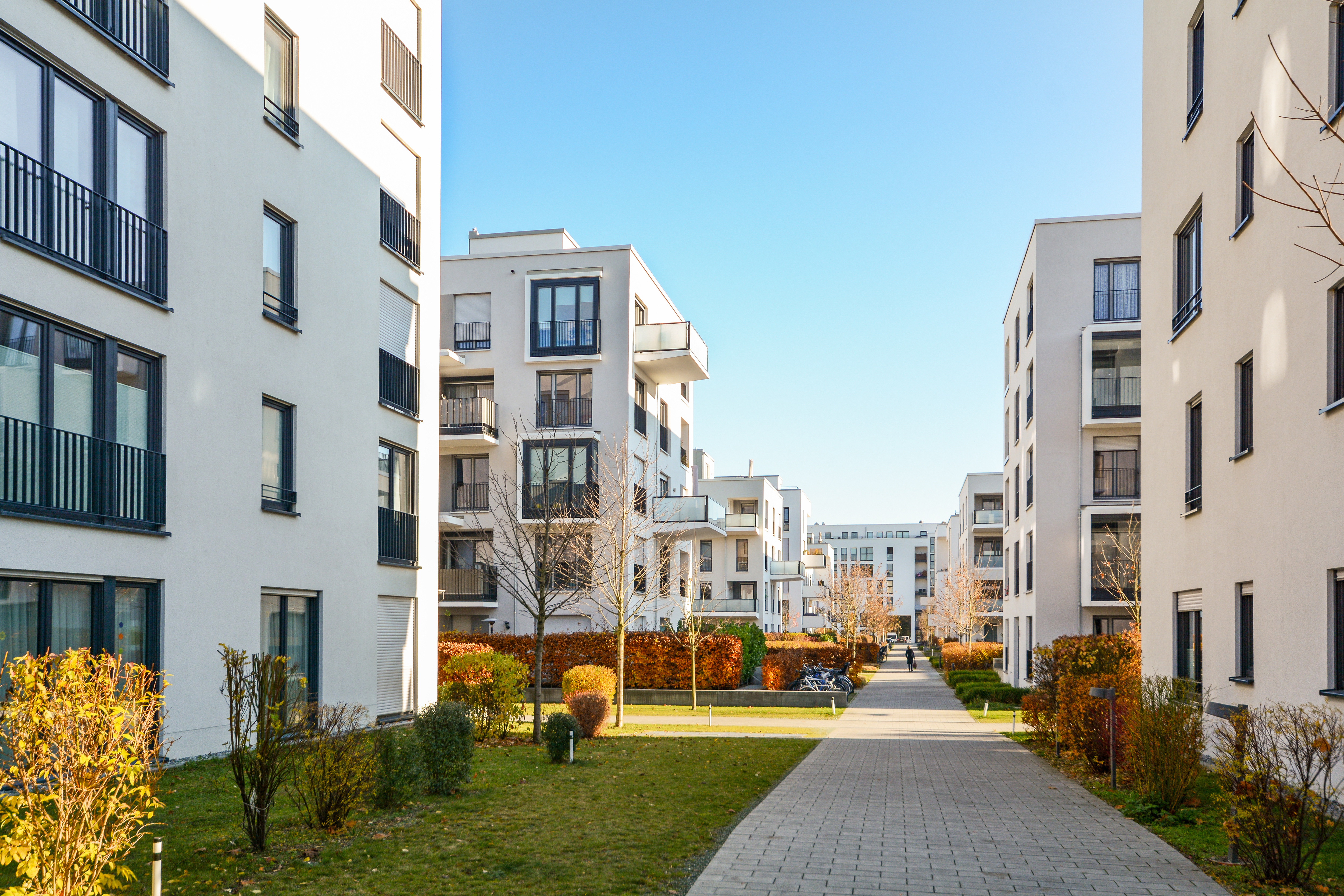 Moderne Wohngebäude mit Balkonen und einem Gehweg dazwischen bei klarem Himmel.
