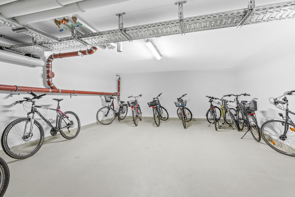 Heller Fahrradkeller mit mehreren abgestellten Fahrrädern und sichtbaren Rohren an der Decke.