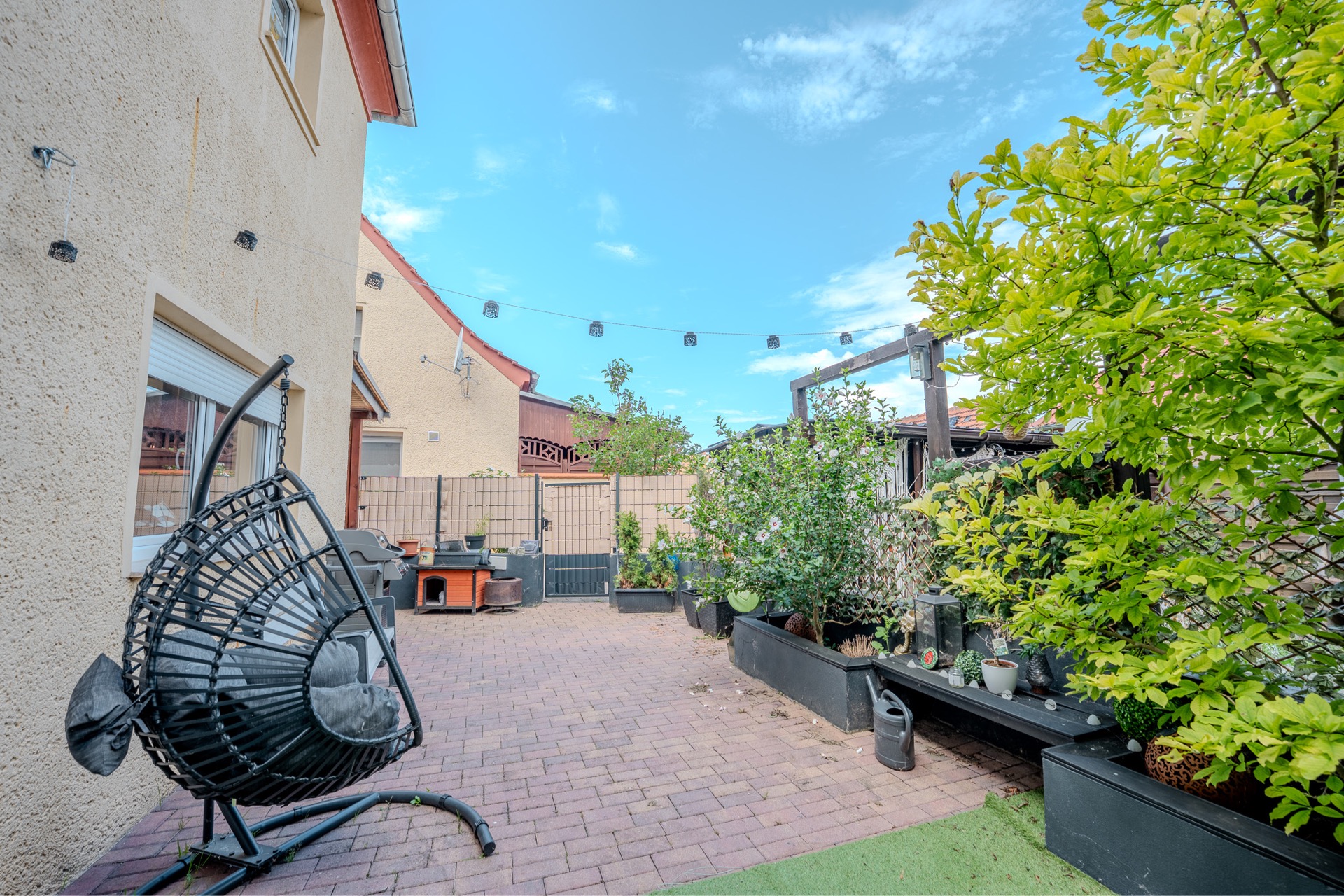 Gepflasterter Innenhof mit Hängekorb-Stuhl, Pflanzen und Gartenmöbeln.