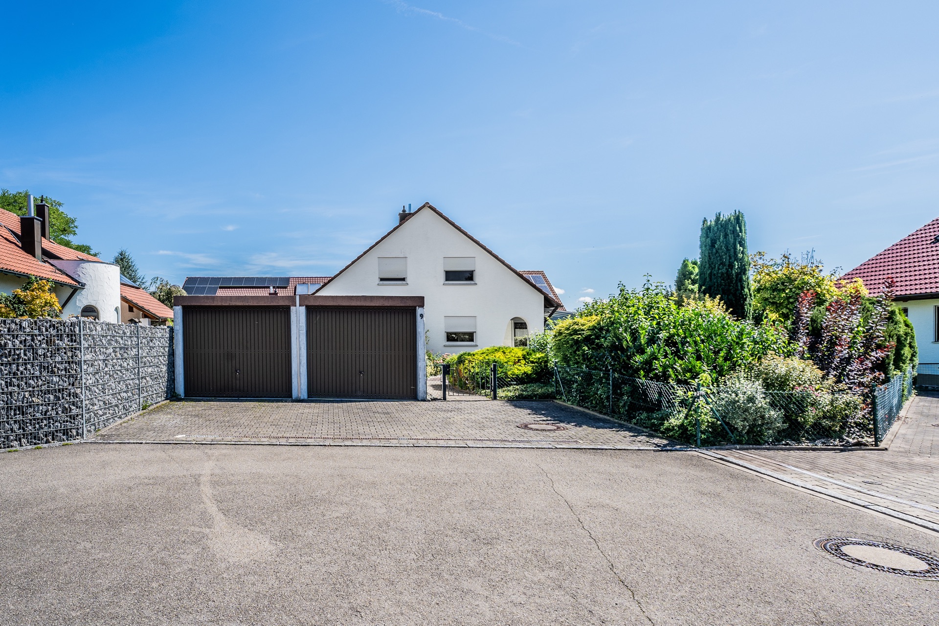 Ein weißes Einfamilienhaus mit zwei Garagen und Garten, aufgenommen von der Straße.