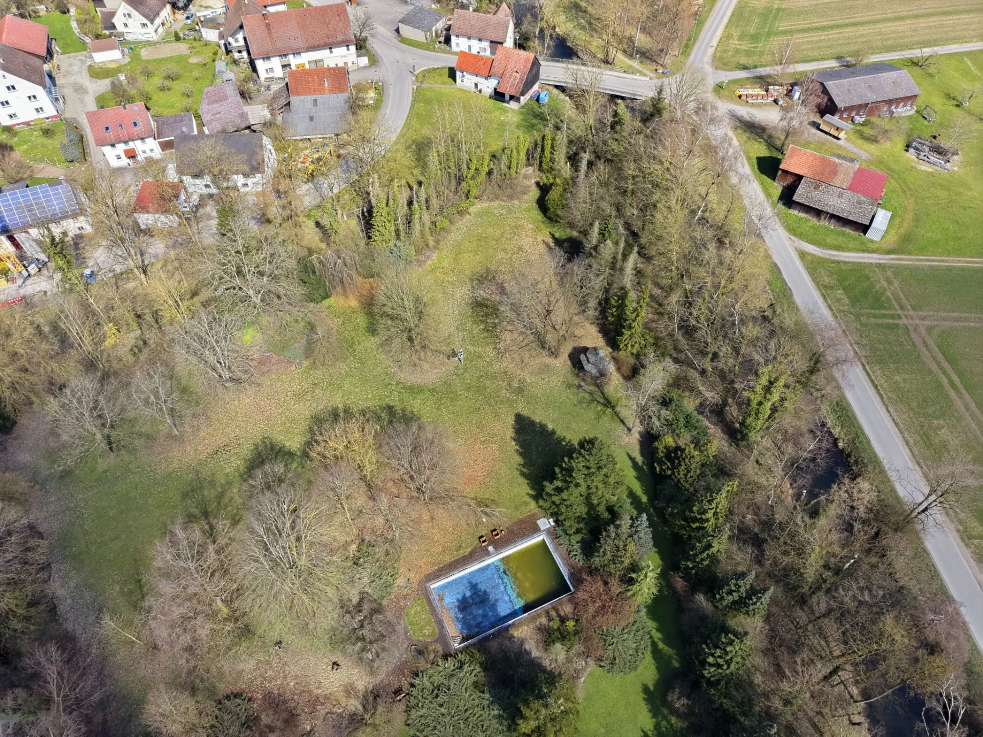 Luftaufnahme eines Grundstücks mit Bäumen, Wiese und rechteckigem Pool in ländlicher Umgebung.