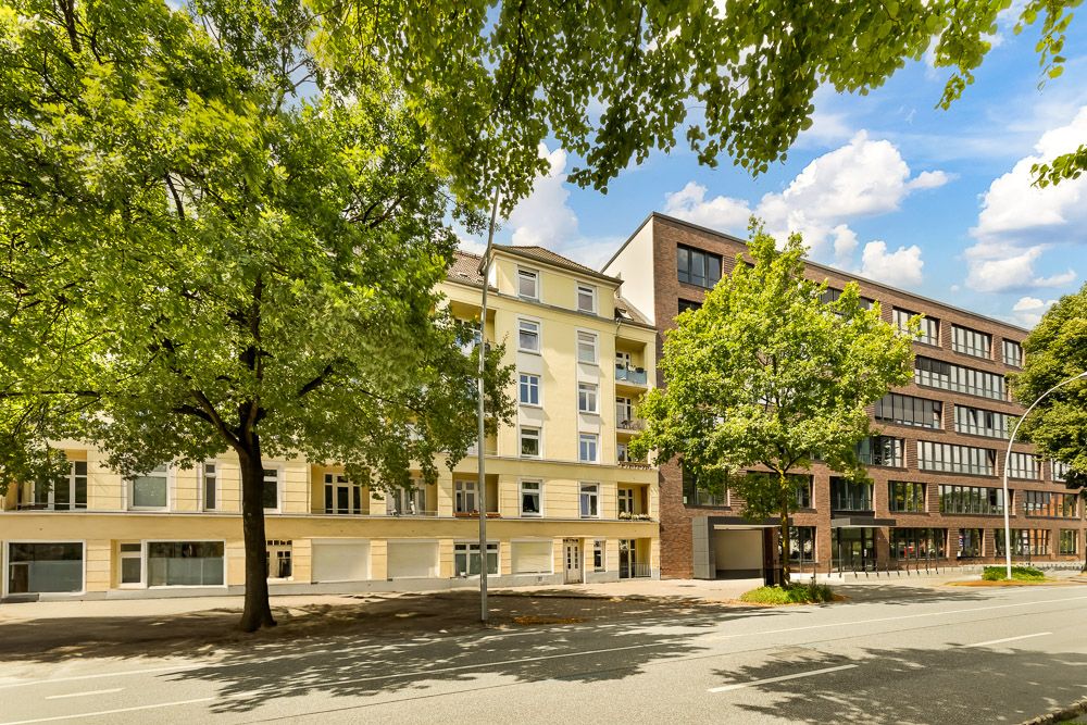 Mehrstöckige Wohngebäude mit Bäumen an einer ruhigen Straße bei sonnigem Wetter.