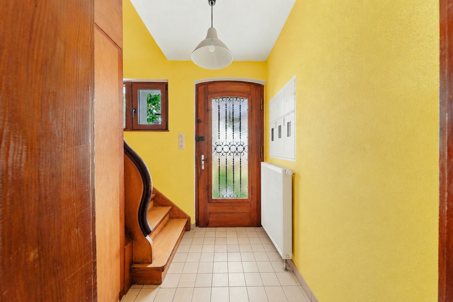 Heller Flur mit gelben Wänden, Holztür, Treppe und kleinem Fenster.