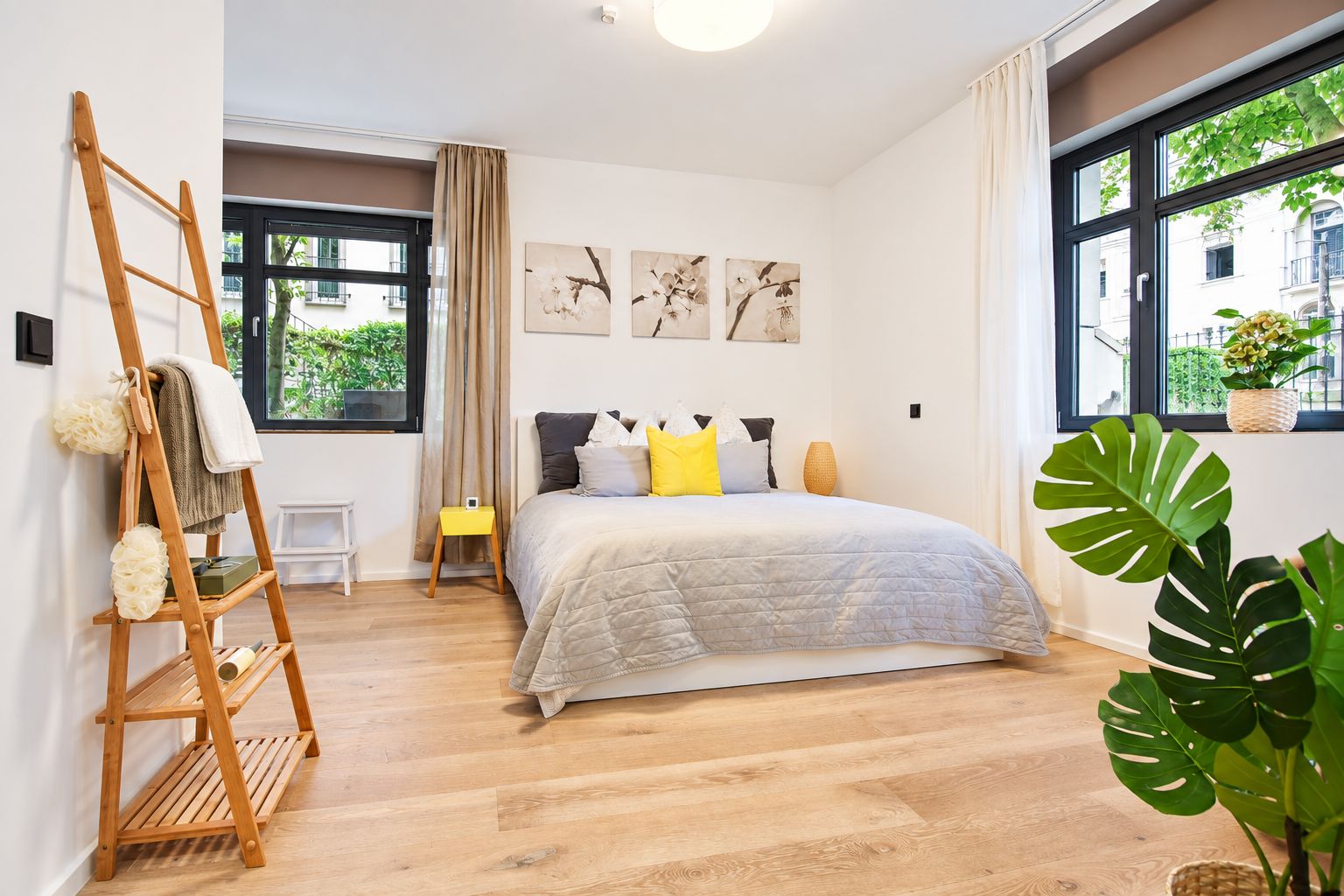 Modernes Schlafzimmer mit Doppelbett, Holzleiterregal, großen Fenstern und Pflanzen auf Holzfußboden.