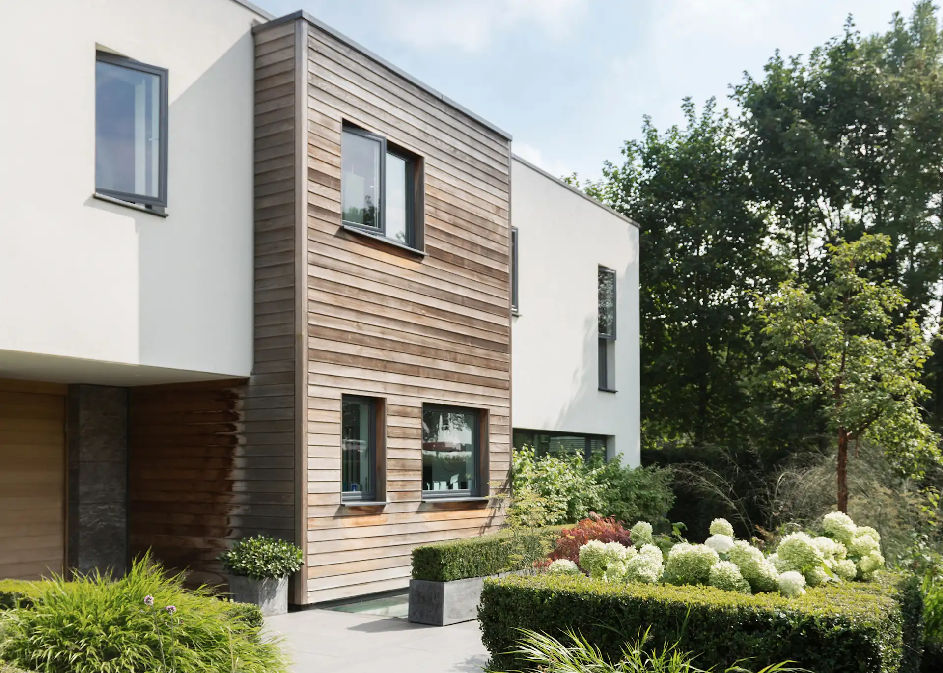 Modernes Wohnhaus mit Holzelementen und gepflegtem Garten im Vordergrund.
