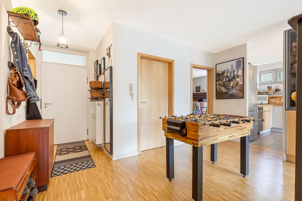 Heller Flur mit Tischkicker, Holzboden, Garderobe und offener Blick in Küche und Wohnbereich.