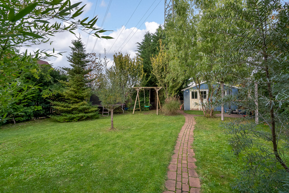 Grüner Garten mit Rasen, Bäumen, Schaukel und einem kleinen Gartenhaus im Hintergrund.
