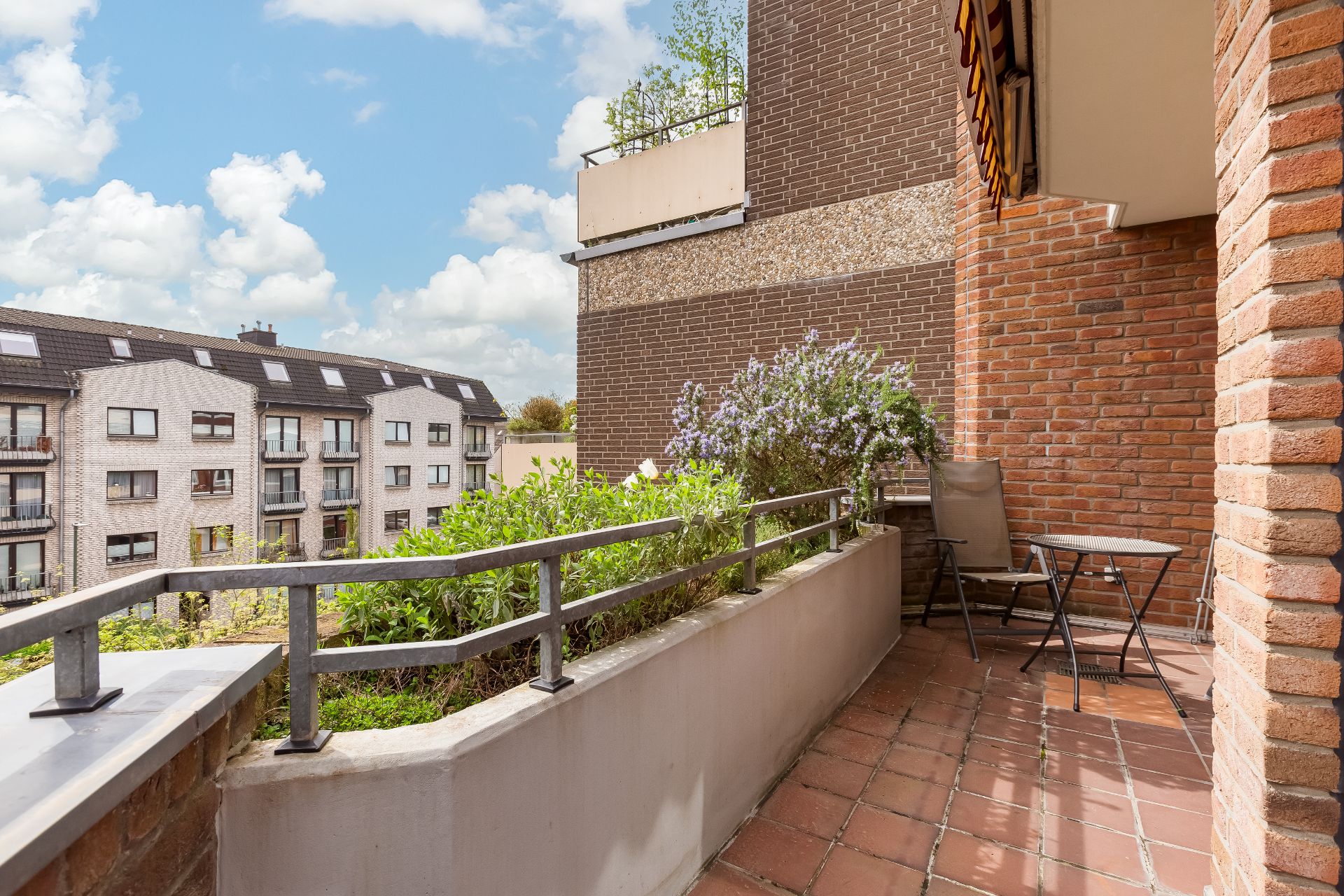Balkon mit Pflanzkübel, Stuhl und kleinem Tisch, Blick auf Wohnhäuser.