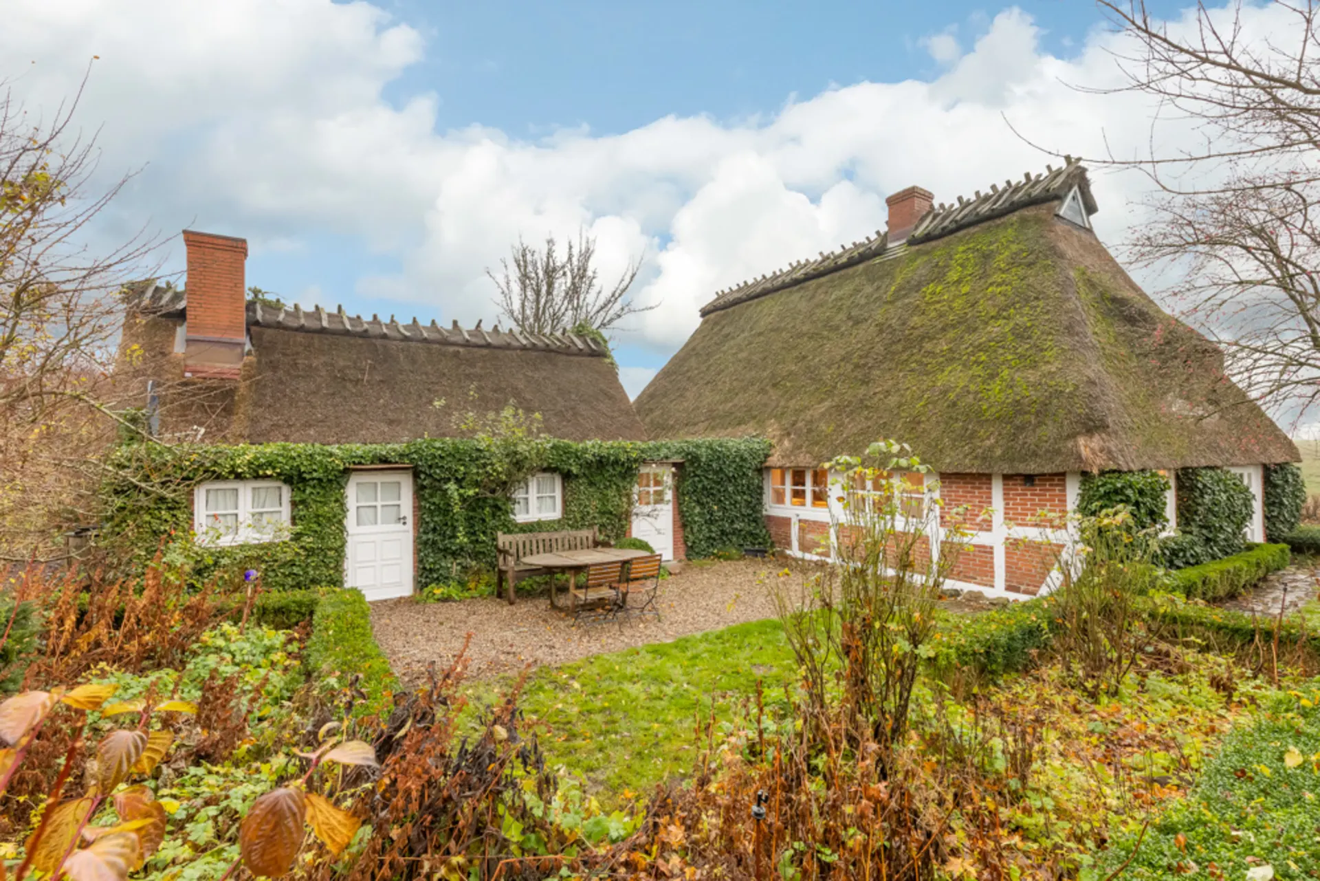 Gemütliches Haus mit Reetdach, Backsteinwänden und Efeubewuchs im Garten.
