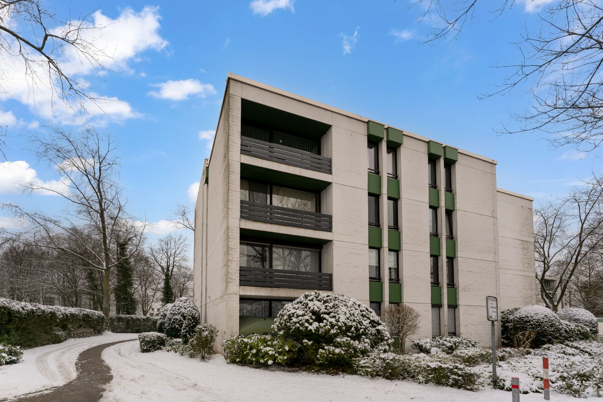 Mehrstöckiges Wohngebäude mit Balkonen und winterlicher Bepflanzung, Weg davor.