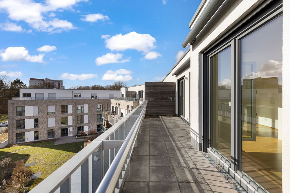 Geräumiger Balkon mit Glasgeländer an einer modernen Wohnanlage bei sonnigem Wetter.