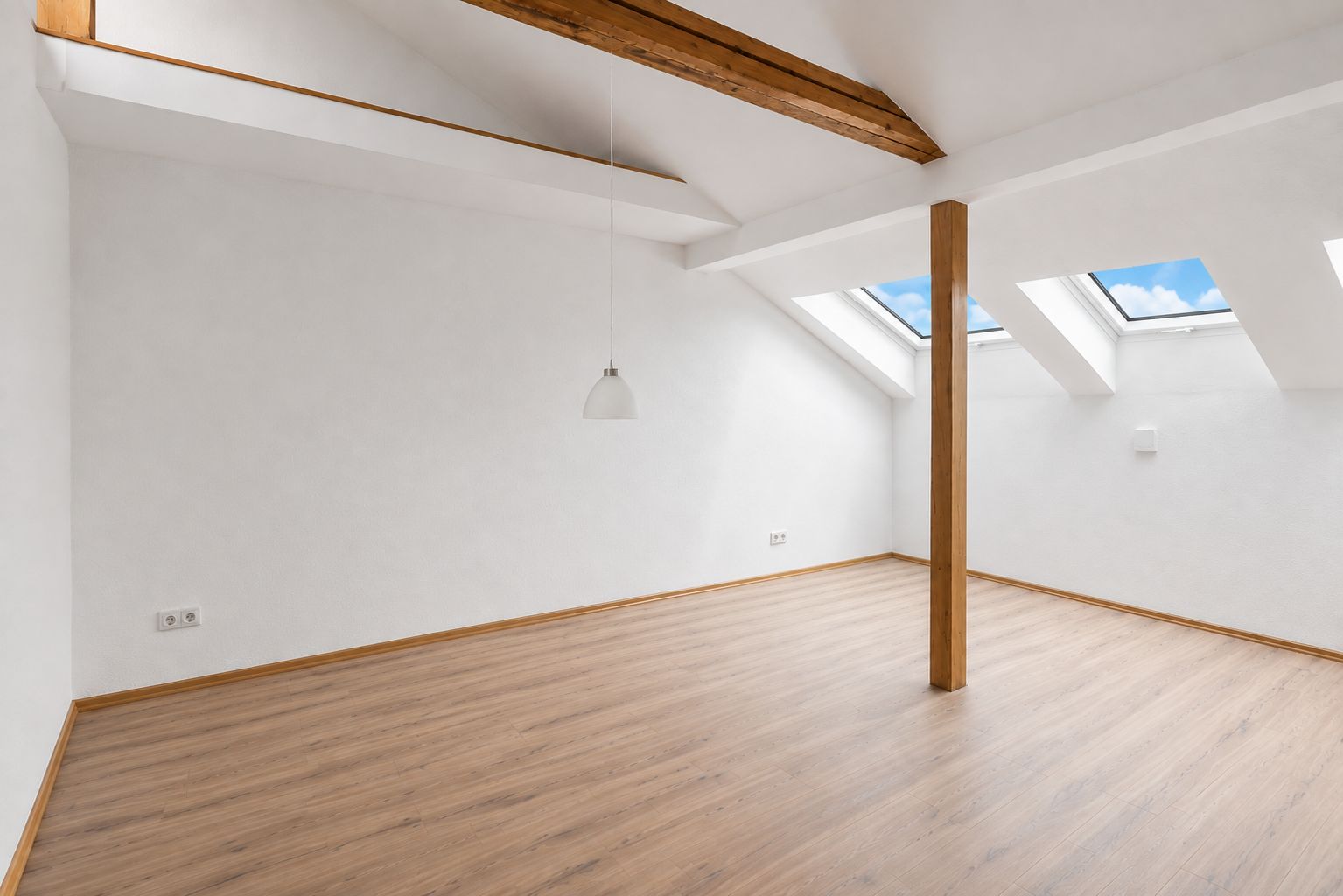 Helles Dachzimmer mit Holzboden, Dachfenstern, Holzbalken und einer Hängelampe.