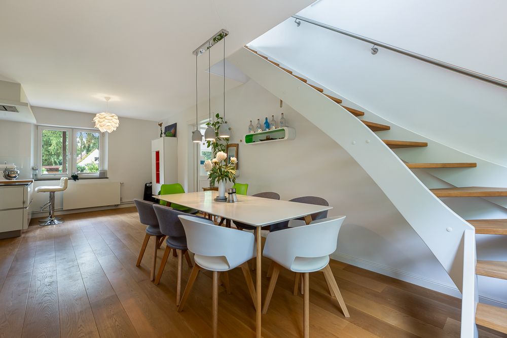Modernes Esszimmer mit Holzboden, Esstisch, bunten Stühlen und Treppe nach oben.