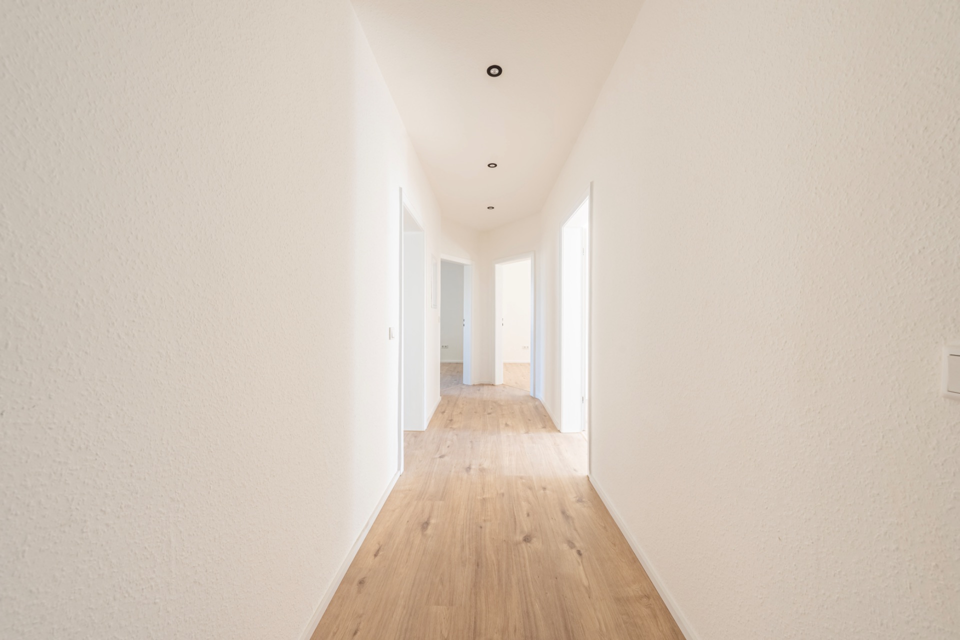 Heller Flur mit Holzfußboden und mehreren offenen Türen in einer Wohnung.