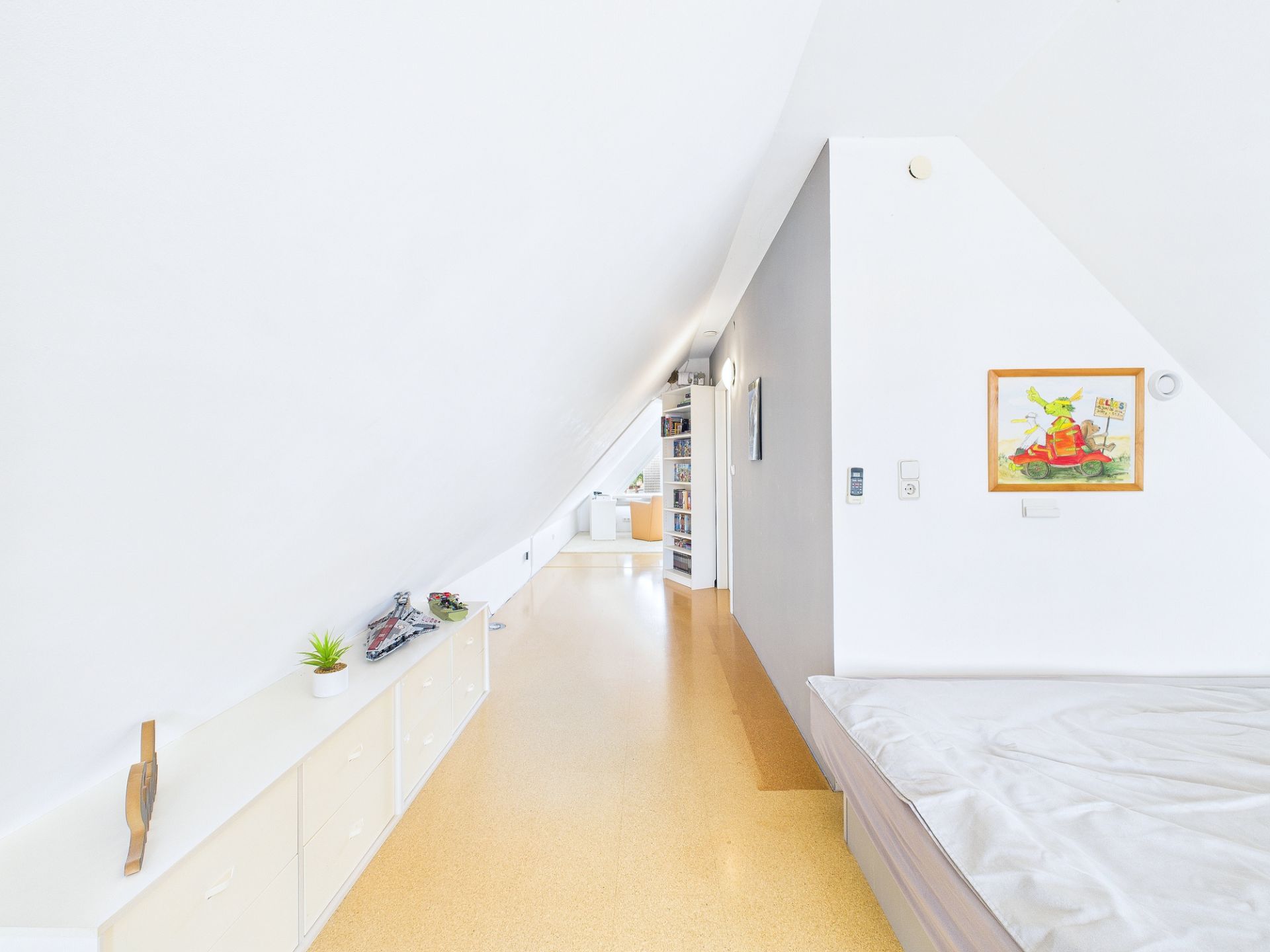 Helles Dachgeschosszimmer mit Bett, weißen Möbeln und schräger Decke.