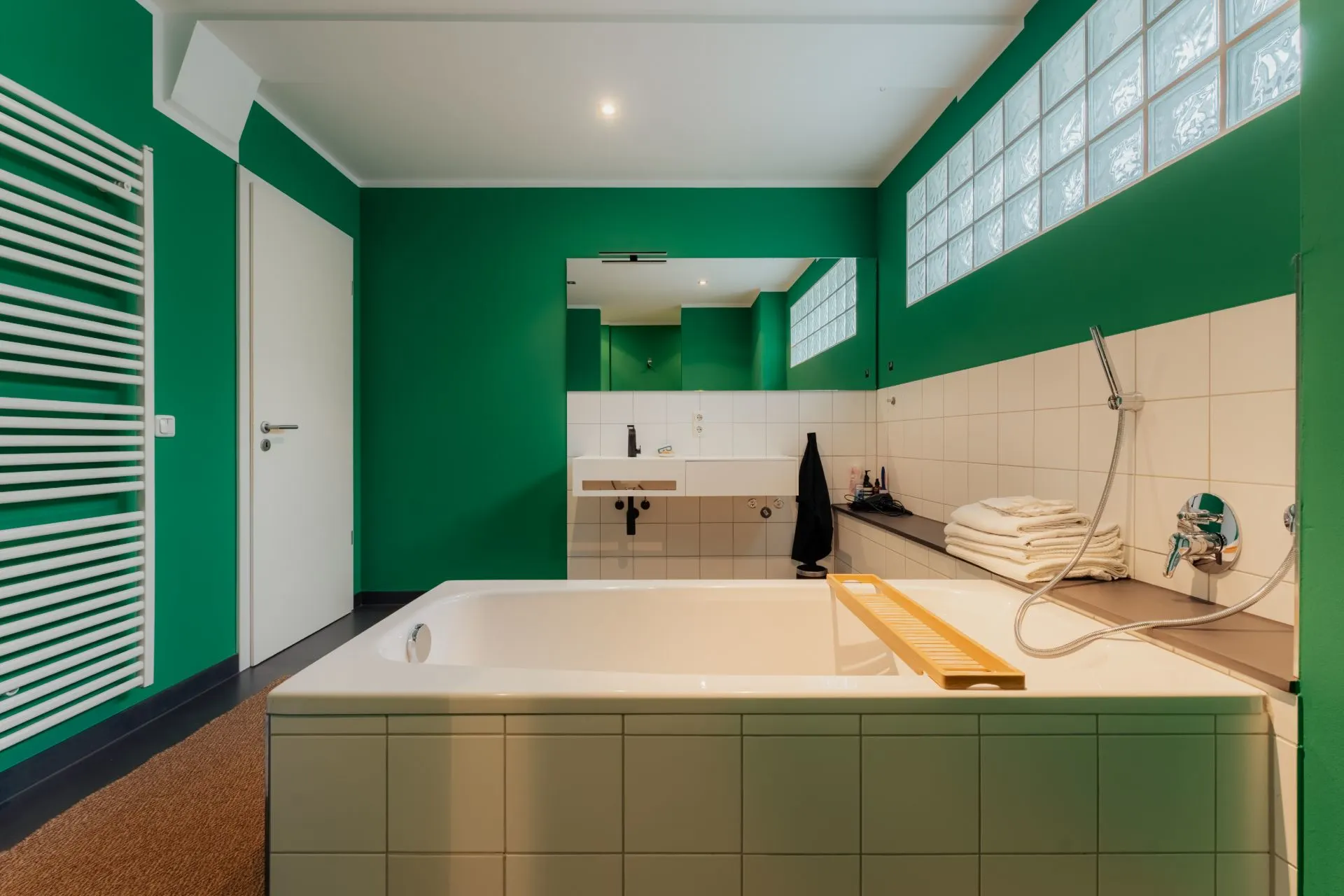 Grünes Badezimmer mit Badewanne, Handtüchern, Waschbecken und großem Spiegel.