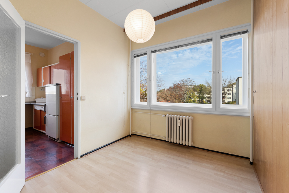 Heller Raum mit großem Fenster, Heizkörper und Zugang zu einer Küche mit rotem Kühlschrank.