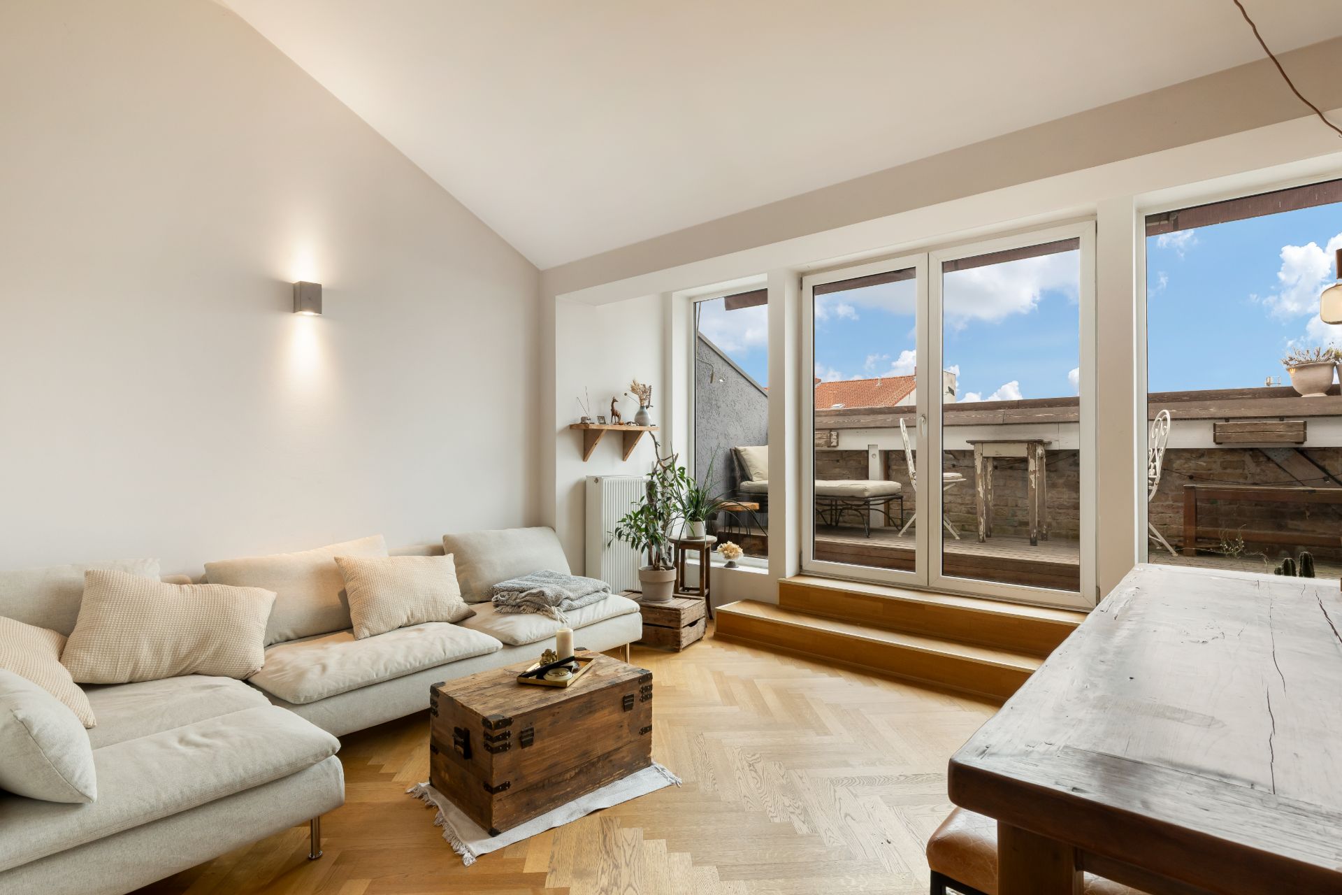 Helles Wohnzimmer mit Sofa, Holztisch und großen Fenstern zu einer Terrasse.