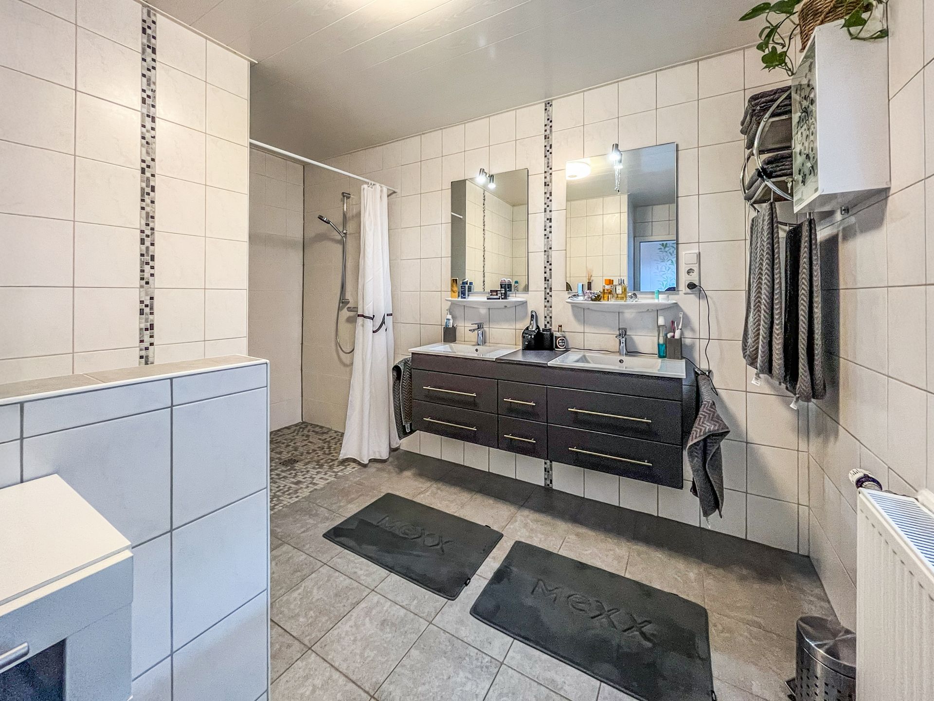 Modernes Badezimmer mit zwei Waschbecken, großer Dusche, Spiegeln und weißen Fliesen.