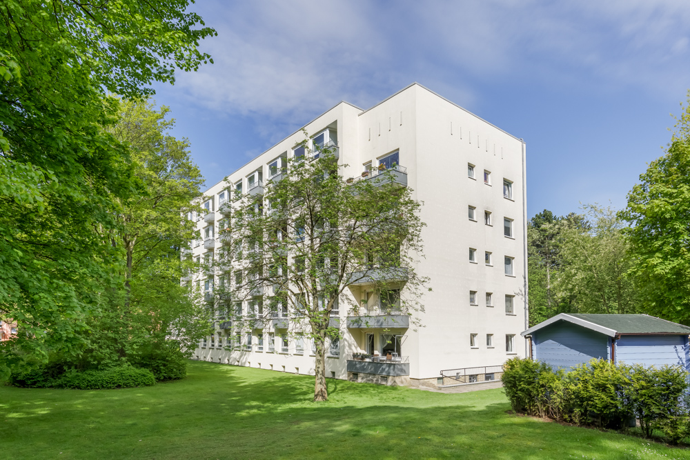 Mehrgeschossiges Wohnhaus mit Balkonen, umgeben von Bäumen und einer großen Wiese.