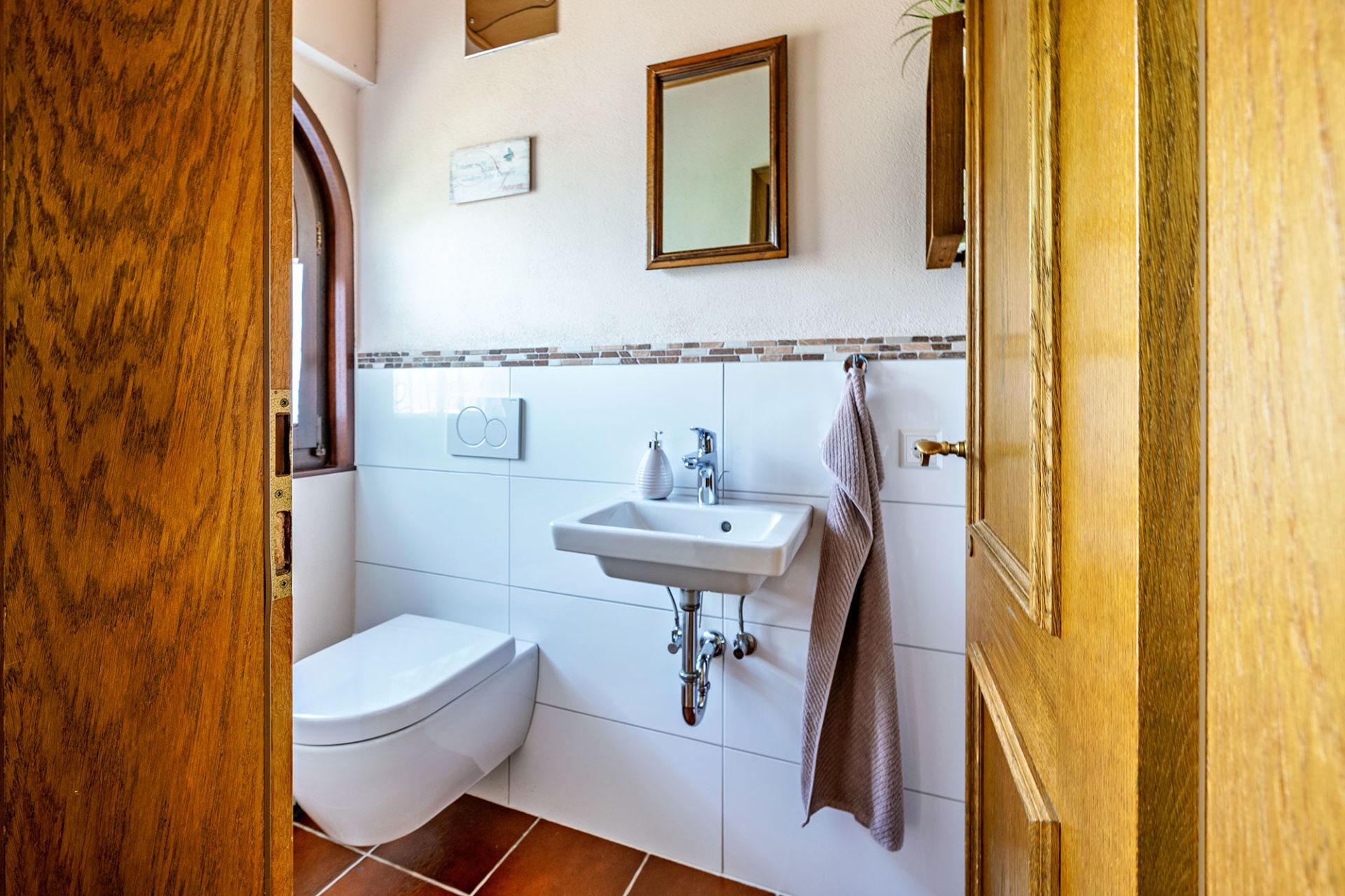Kleines Bad mit Wandtoilette, Waschbecken, Spiegel und Handtuch.
