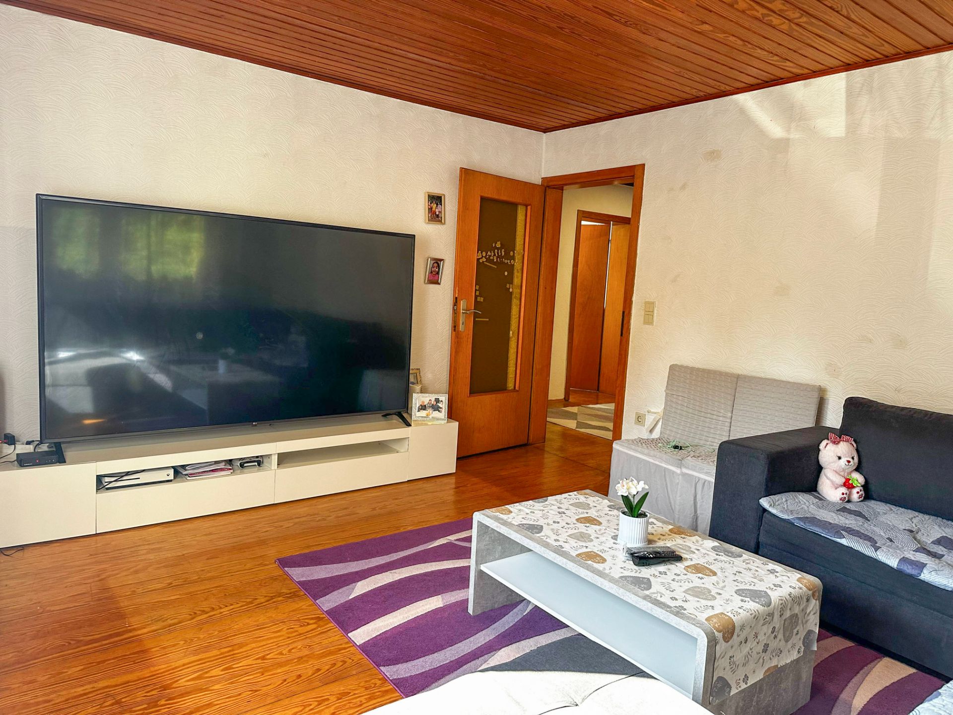 Wohnzimmer mit großem Fernseher, Sofa, Couchtisch und lila Teppich.