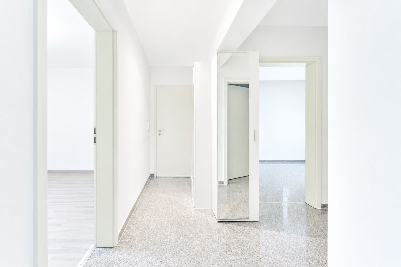 Heller Flur mit Spiegelkleiderschrank, mehreren Türen und grauem Boden.