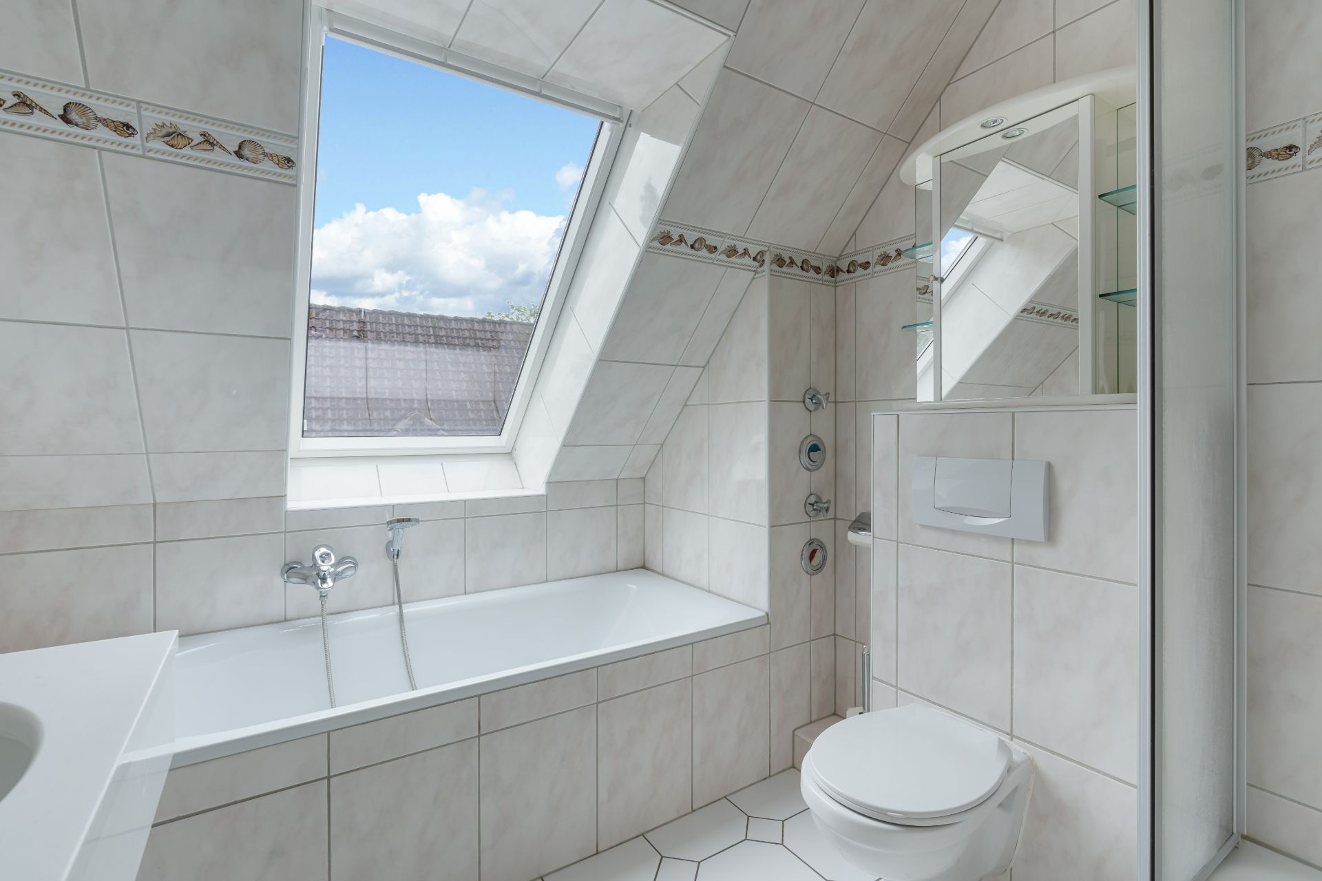 Helles Badezimmer mit Badewanne, Dachfenster, Toilette und Spiegel.