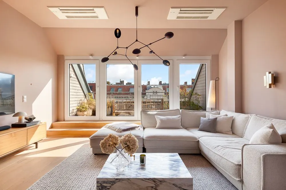 Helles Wohnzimmer mit großem Ecksofa, Couchtisch, Fernseher und großen Fenstern zur Terrasse.