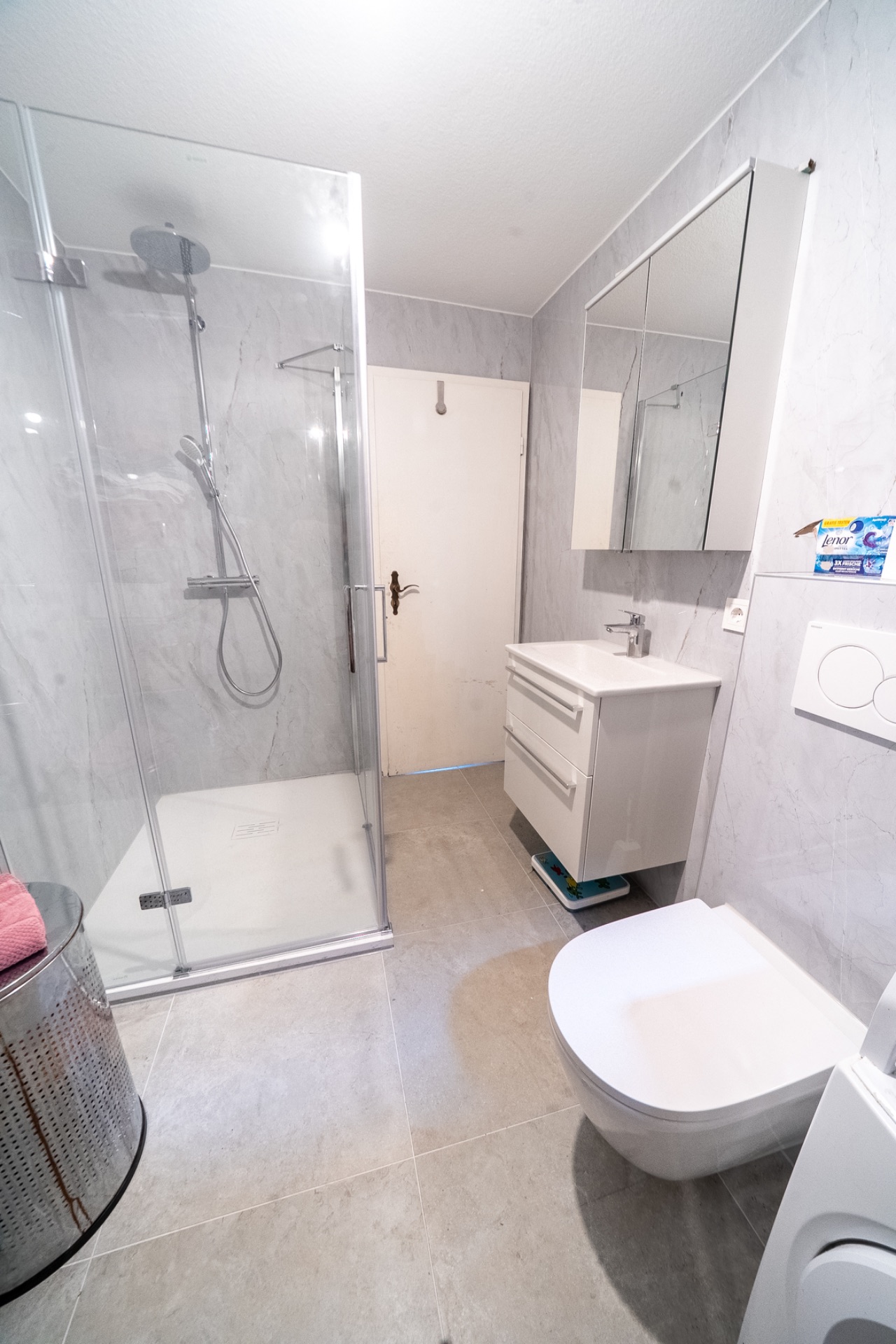 Modernes Bad mit Dusche, Waschbecken, Spiegelschrank und Toilette.