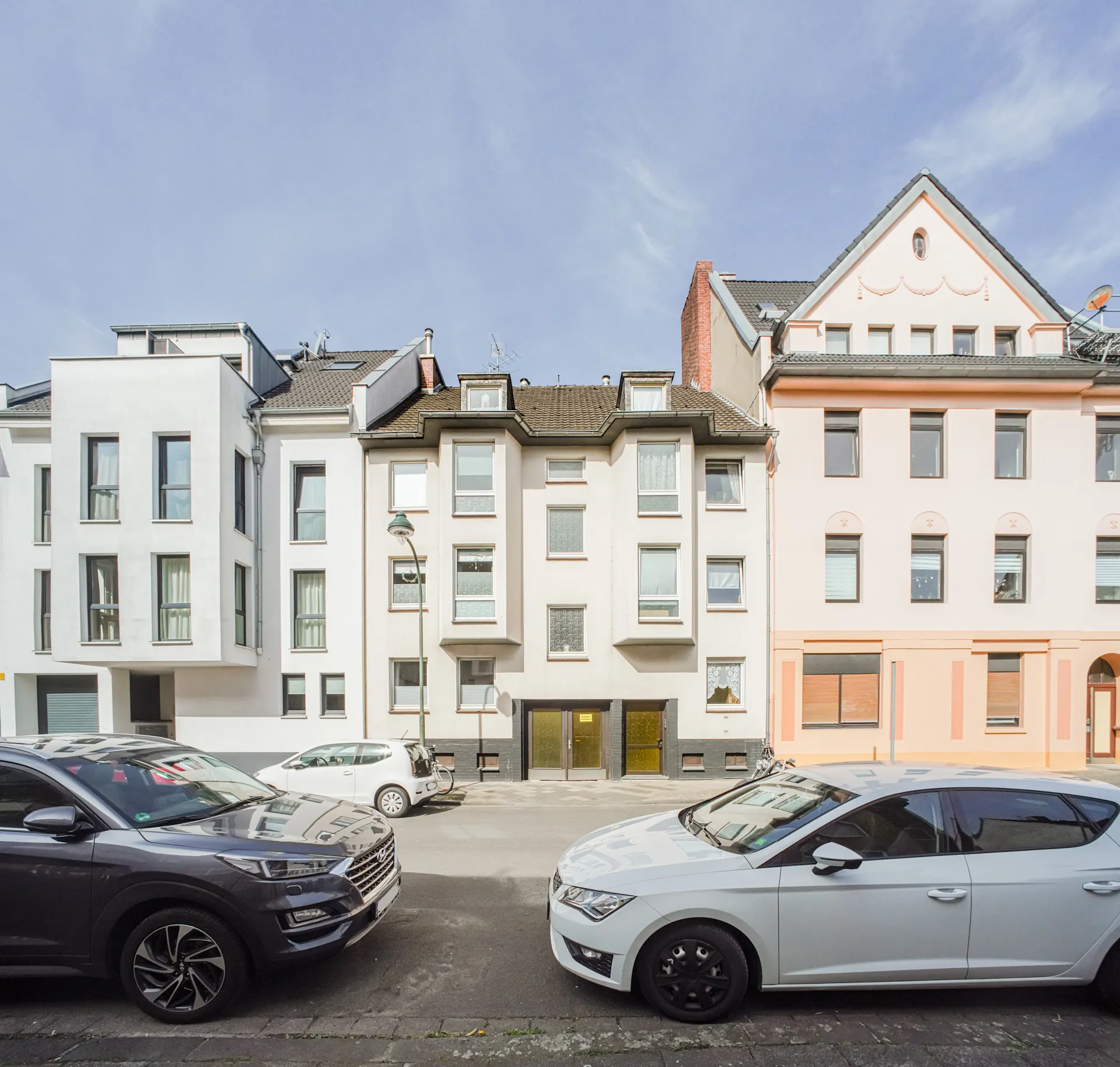Mehrfamilienhäuser mit geparkten Autos auf der Straße bei Tageslicht.