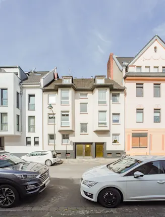 Mehrfamilienhäuser mit geparkten Autos auf der Straße bei Tageslicht.