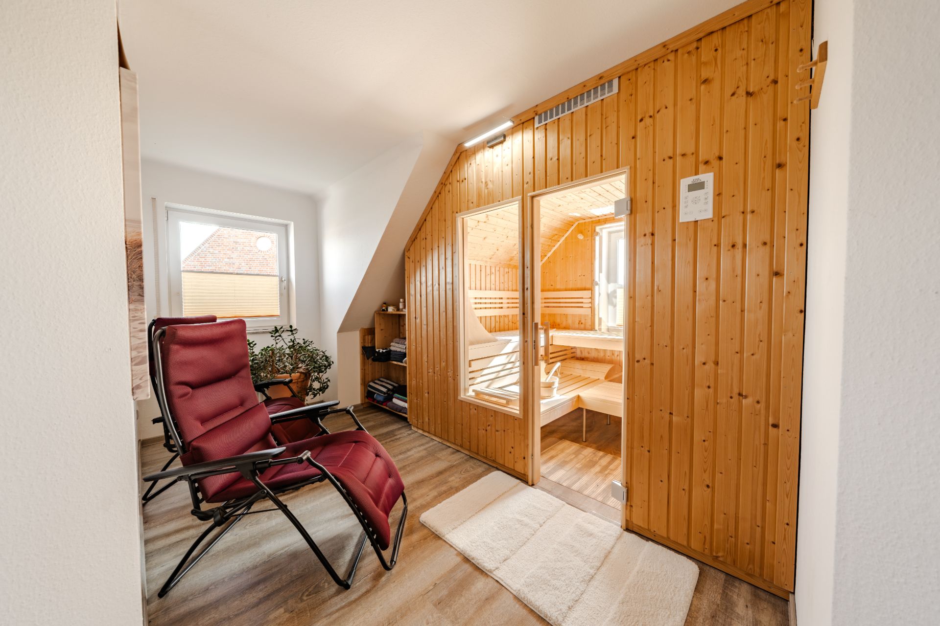 Raum mit zwei roten Liegestühlen und einer Sauna aus Holz an der Wand.