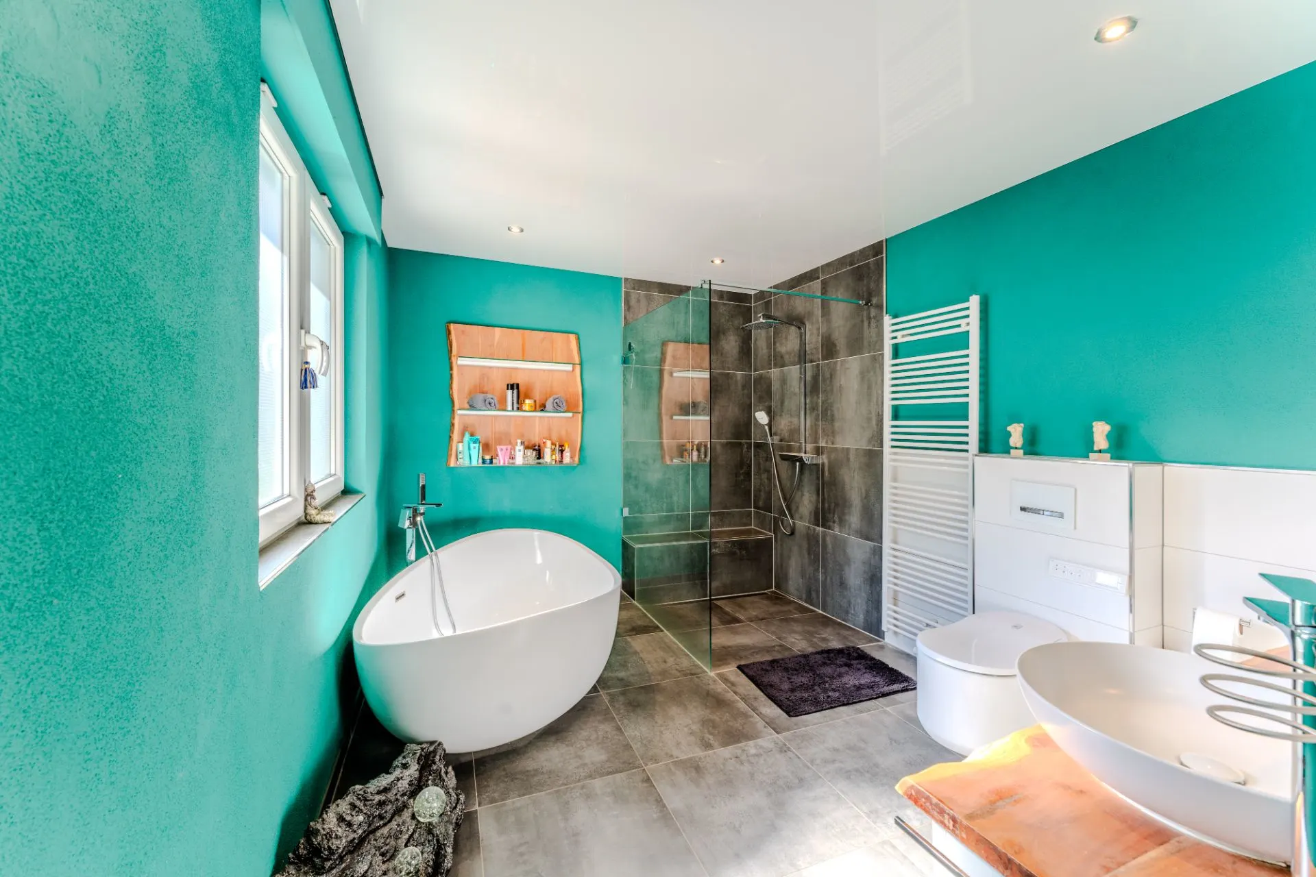 Modernes Bad mit freistehender Badewanne, bodengleicher Dusche und türkisfarbenen Wänden.