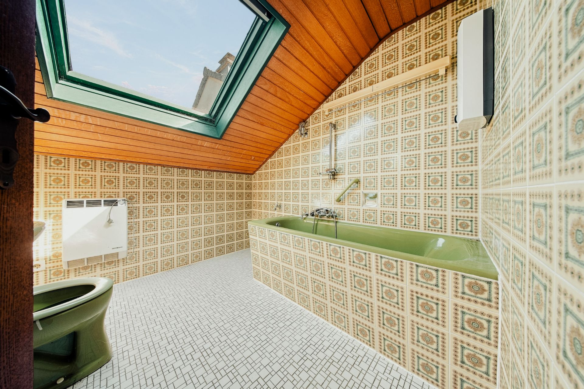 Badezimmer mit grüner Badewanne, WC, gemusterten Fliesen und Dachfenster.