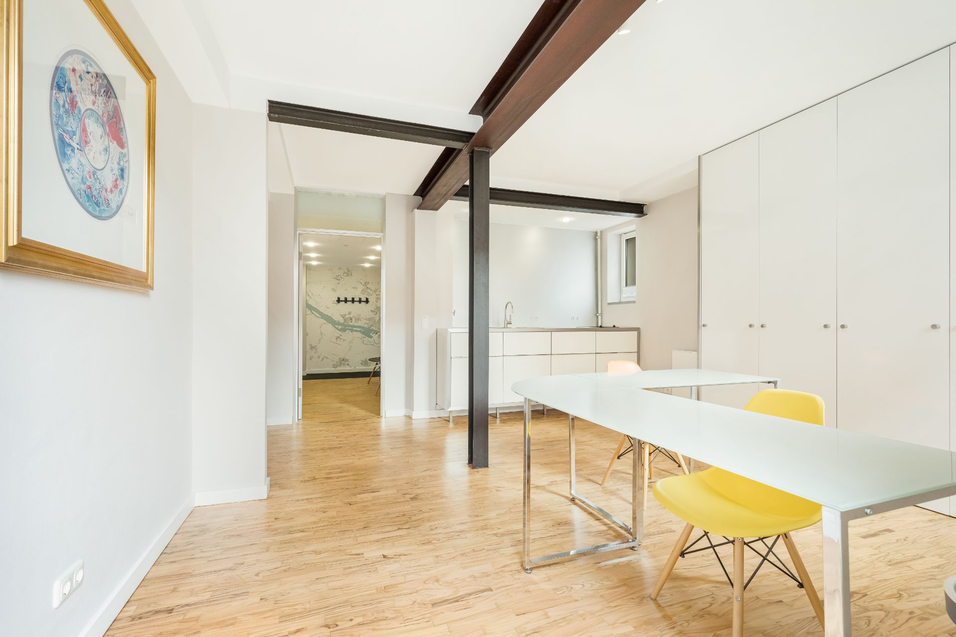 Heller Raum mit Holzboden, Glastisch, gelben Stühlen und weißem Einbauschrank.