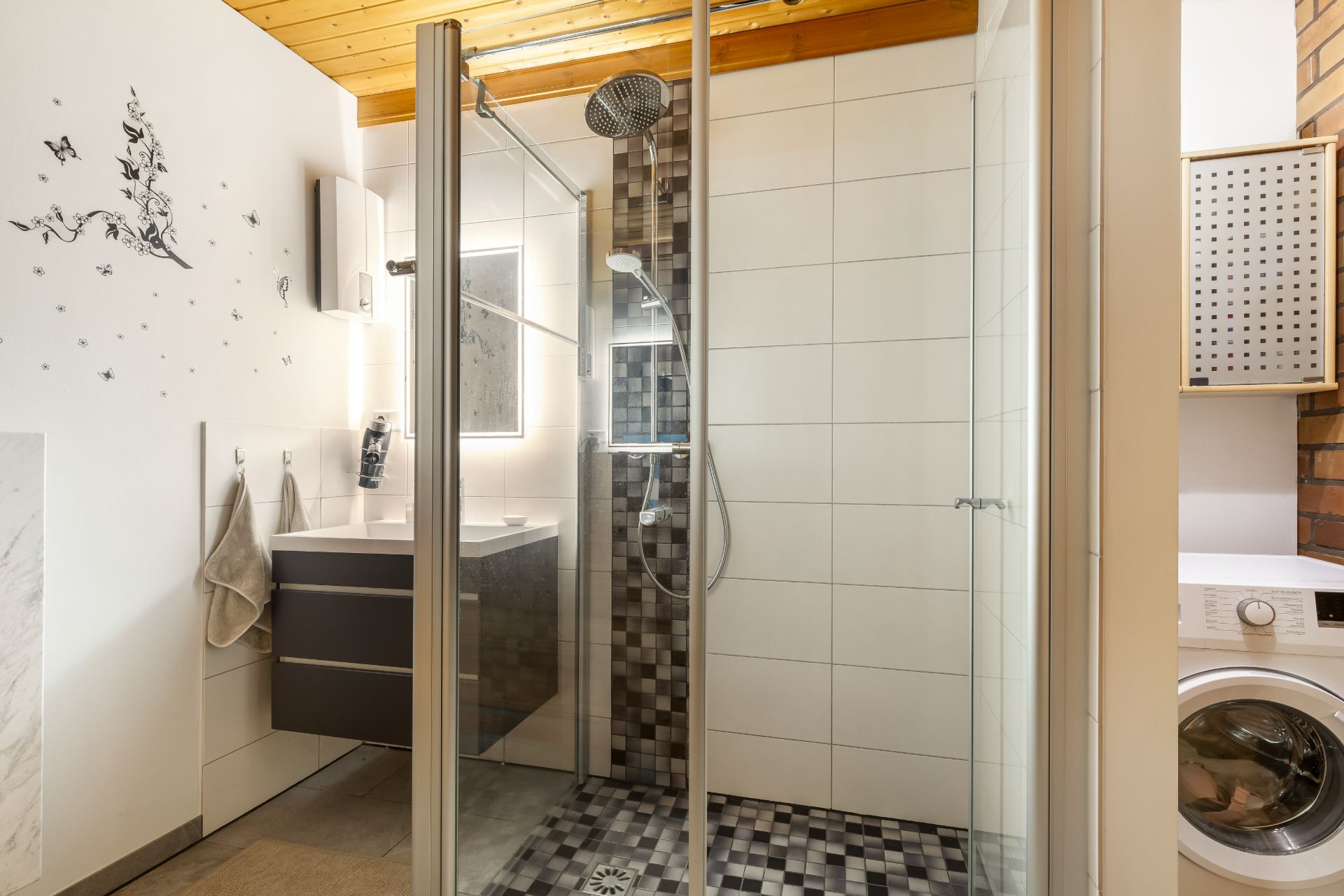 Modernes Bad mit ebenerdiger Dusche, Waschbecken, Waschmaschine und Dekoration an der Wand.