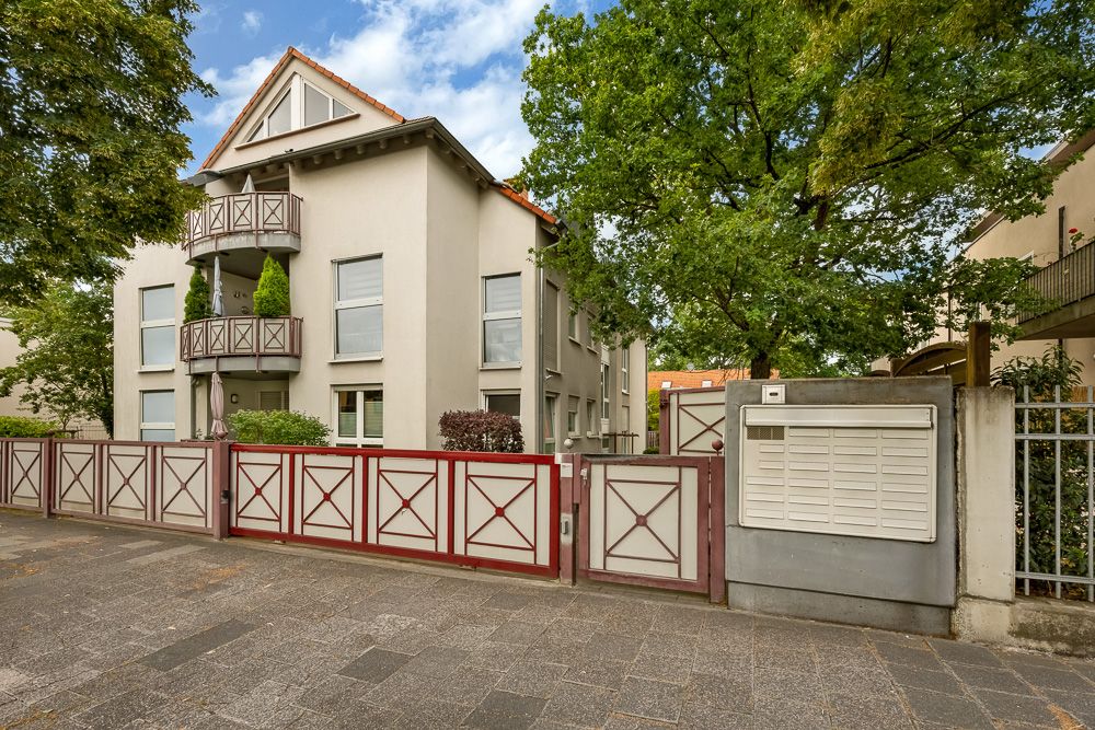 Zweistöckiges Wohnhaus mit Balkon, Vorgarten und Holz-Zaun, umgeben von Bäumen.