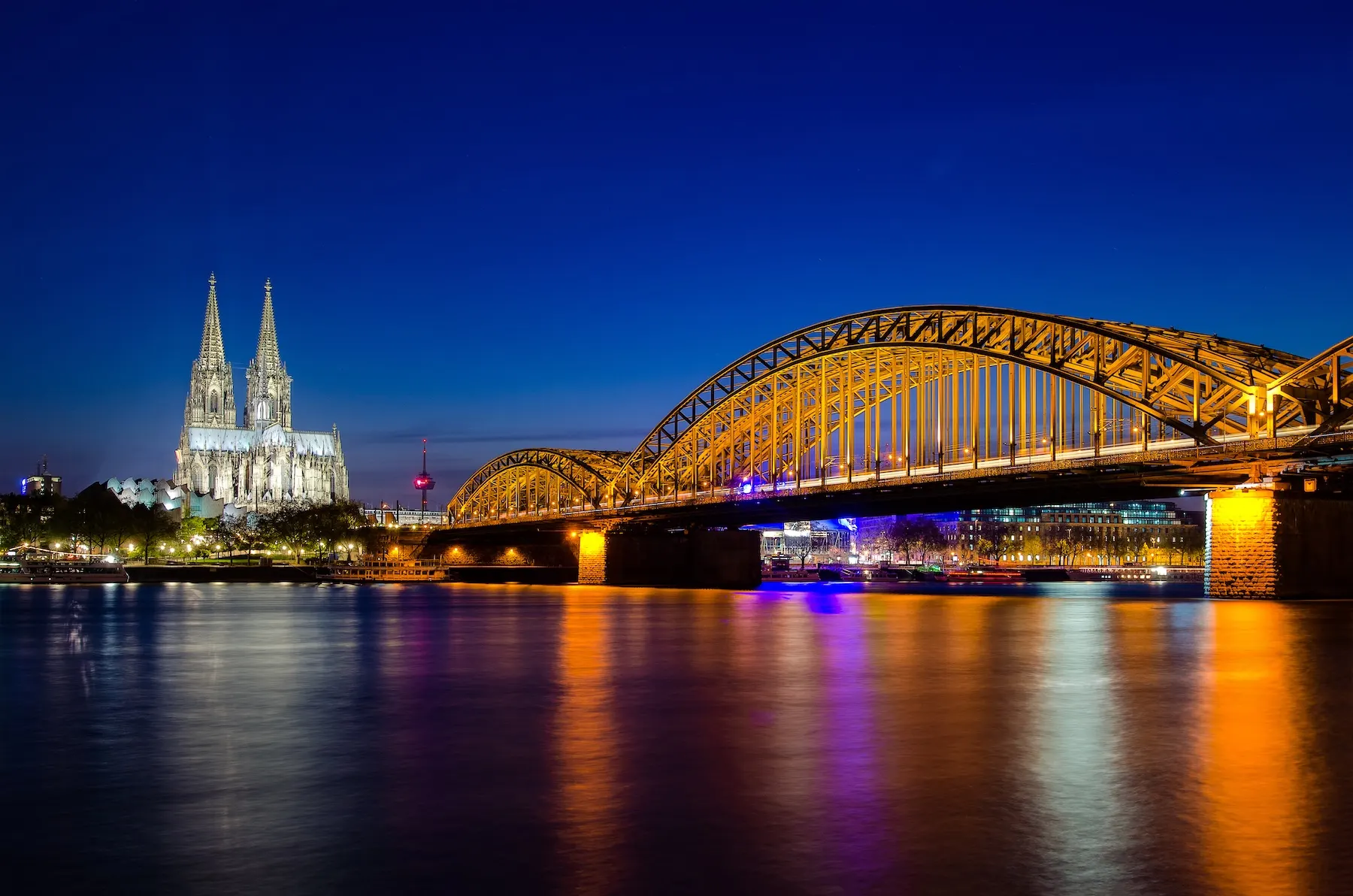 Beleuchtete Brücke über einen Fluss bei Nacht, im Hintergrund eine große Kathedrale.