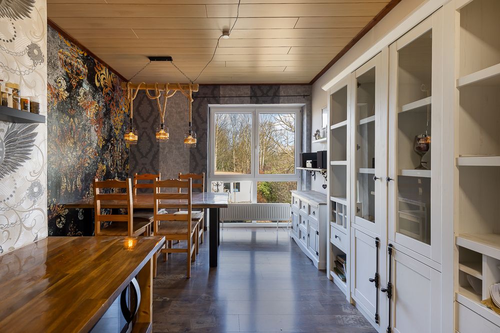 Esszimmer mit Holztisch, Stühlen, weißen Vitrinenschränken und großem Fenster mit Ausblick.