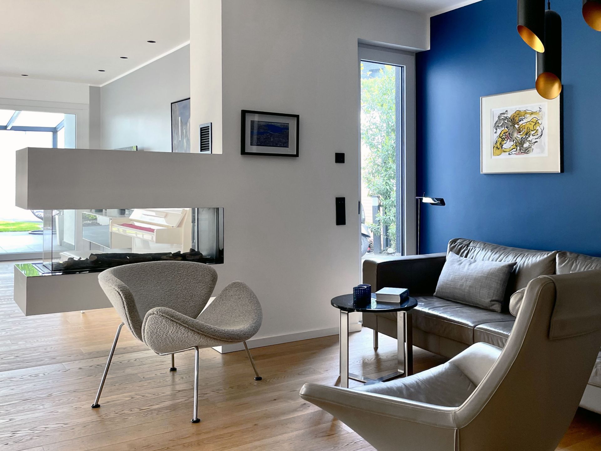 Modernes Wohnzimmer mit Sesseln, Sofa, Kamin, blauer Wand und großem Fenster.